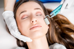 a beautiful woman having a licensed esthetician give her a microneedling treatment